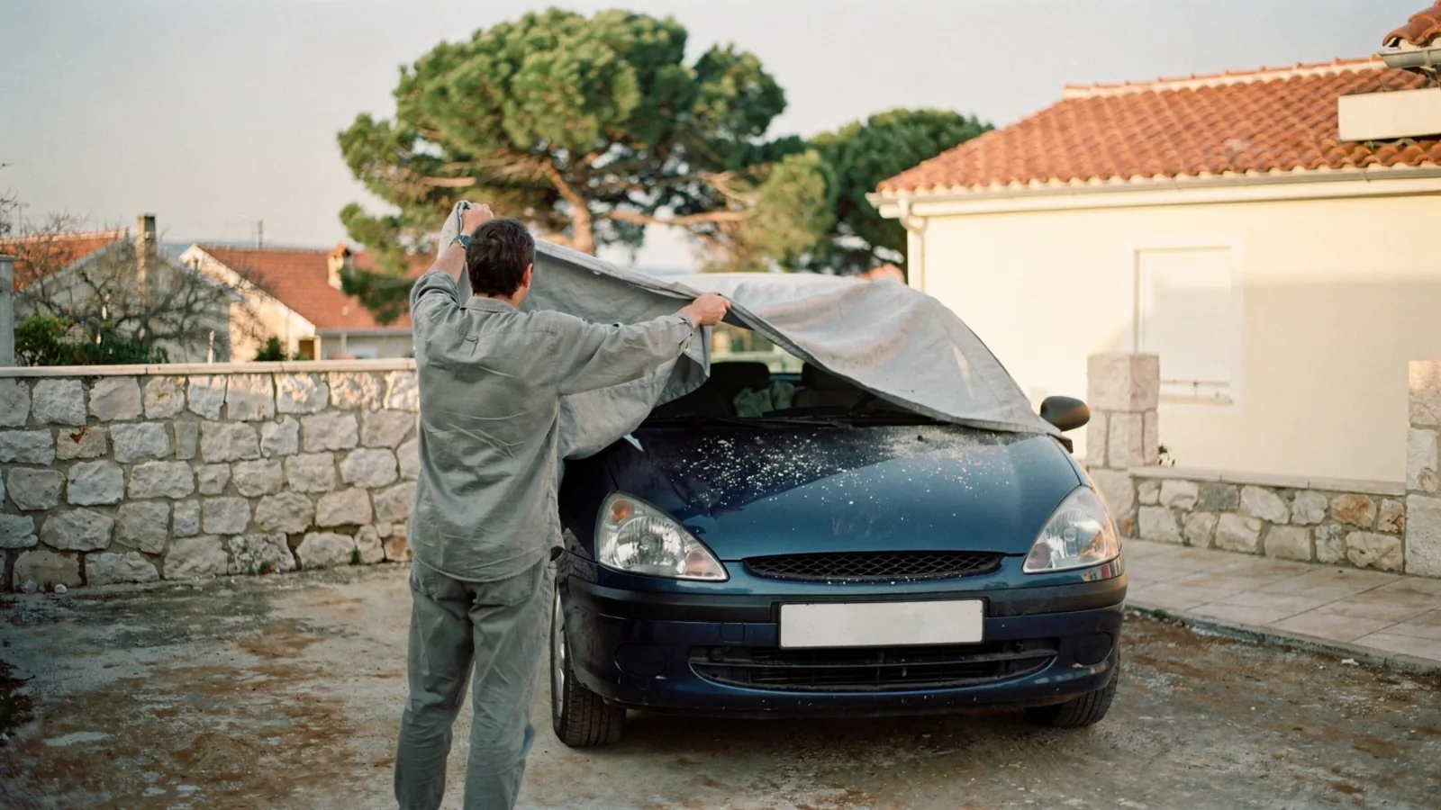 Skidanje zaprašene zaštitne navlake s automobila parkiranog ispred obiteljske kuće na obali